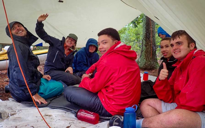 a group of teens rest under a tarp on an outward bound expedition 